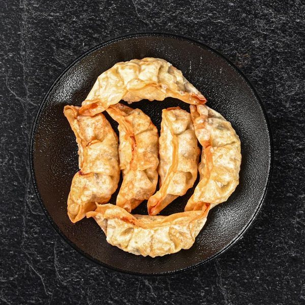 Fem stegte gyoza på en sort tallerken.