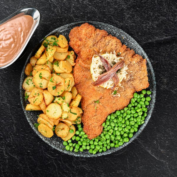 Paneret schnitzel med kartofler, ærter og garniture.